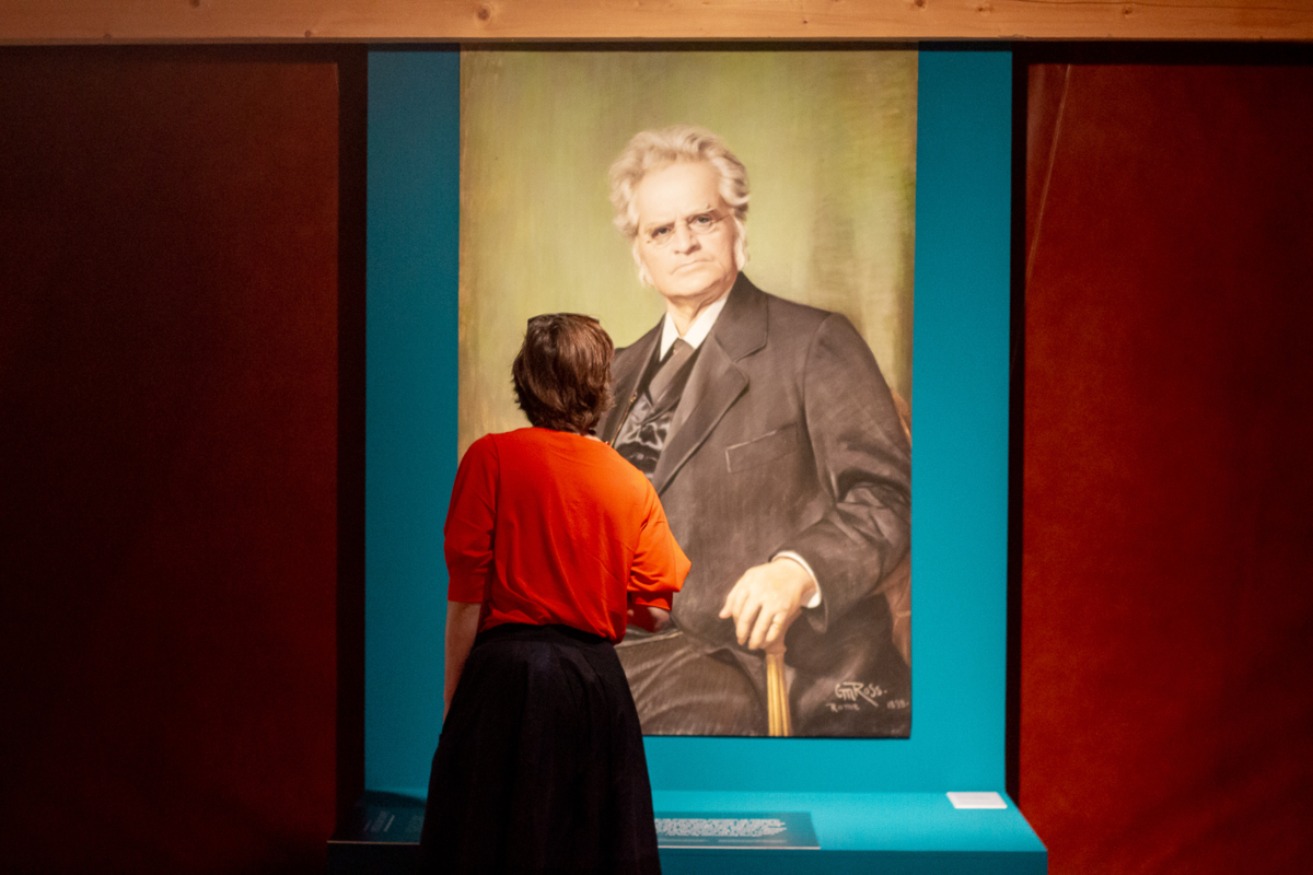 Dame studerer bilde av Bjørnstjerne Bjørnson i utstillingen Det volder litt rabalder.